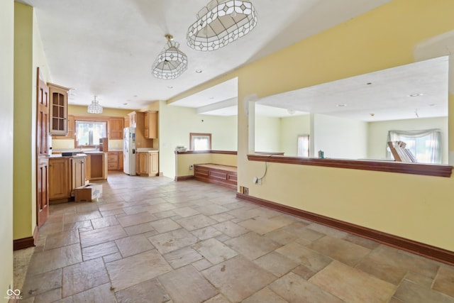 kitchen featuring stone tile flooring, open floor plan, white refrigerator with ice dispenser, and baseboards