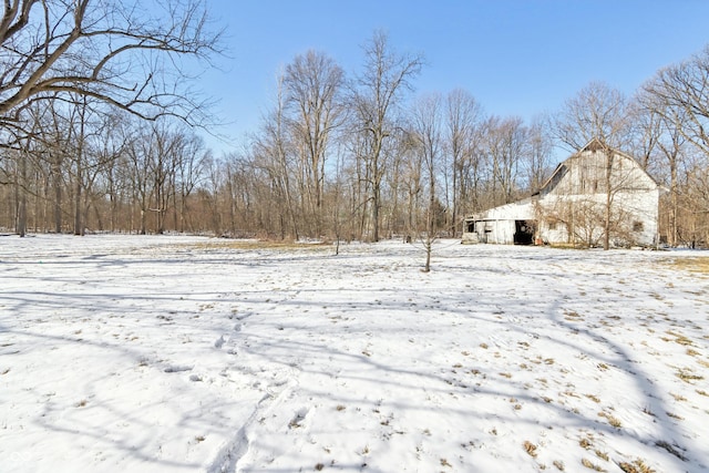 yard layered in snow with a barn, an outdoor structure, and a detached garage