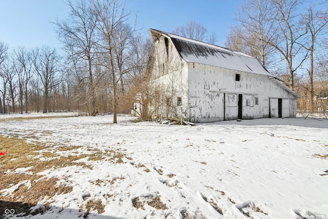 view of snowy exterior featuring a gambrel roof, a barn, a detached garage, and an outdoor structure