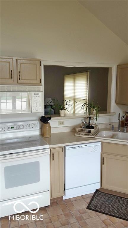 kitchen featuring lofted ceiling, white appliances, light countertops, and a sink