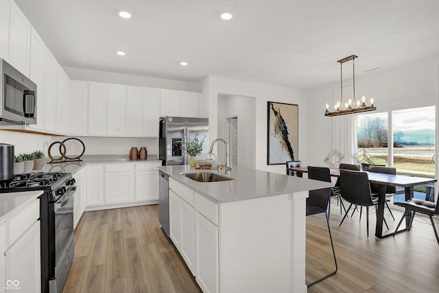 kitchen featuring stainless steel appliances, a sink, white cabinets, light countertops, and a center island with sink