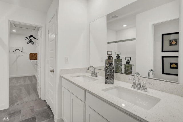 bathroom featuring a walk in closet, visible vents, a sink, and double vanity