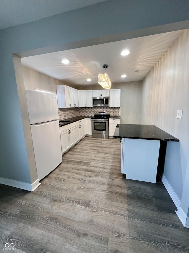 kitchen featuring stainless steel appliances, dark countertops, backsplash, white cabinets, and a peninsula