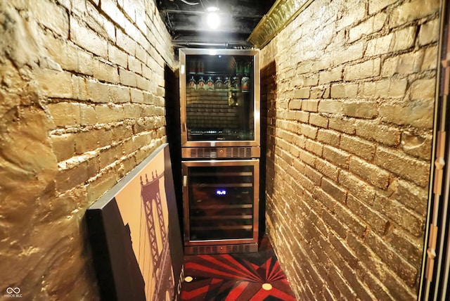 wine room featuring a bar, brick wall, and beverage cooler