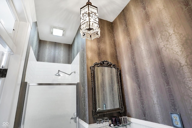 bathroom featuring a chandelier, a shower with door, and wallpapered walls