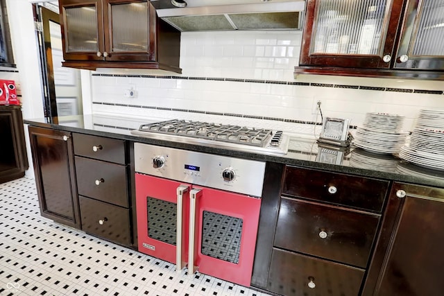 kitchen featuring glass insert cabinets, range hood, dark brown cabinets, stainless steel gas cooktop, and backsplash