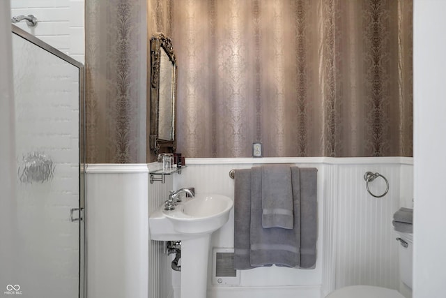 bathroom featuring a sink, a wainscoted wall, wallpapered walls, and a stall shower