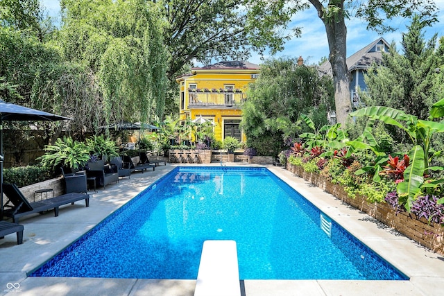 pool with a patio area, fence, and a diving board