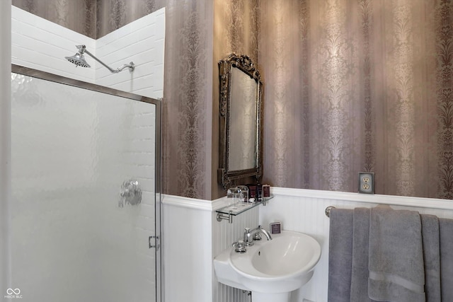 bathroom featuring a wainscoted wall, a stall shower, a sink, and wallpapered walls