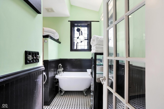 full bathroom featuring a freestanding tub, a wainscoted wall, visible vents, and vaulted ceiling