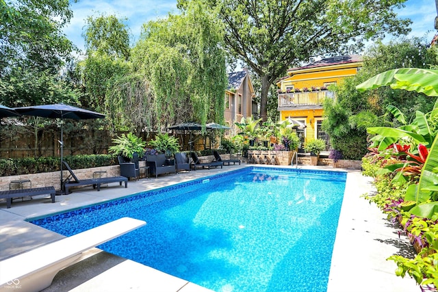 pool with a patio area, fence, and a diving board