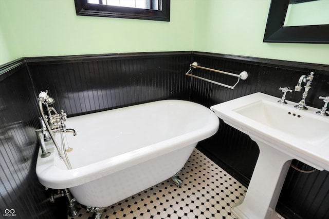 bathroom with a soaking tub, wainscoting, and a sink