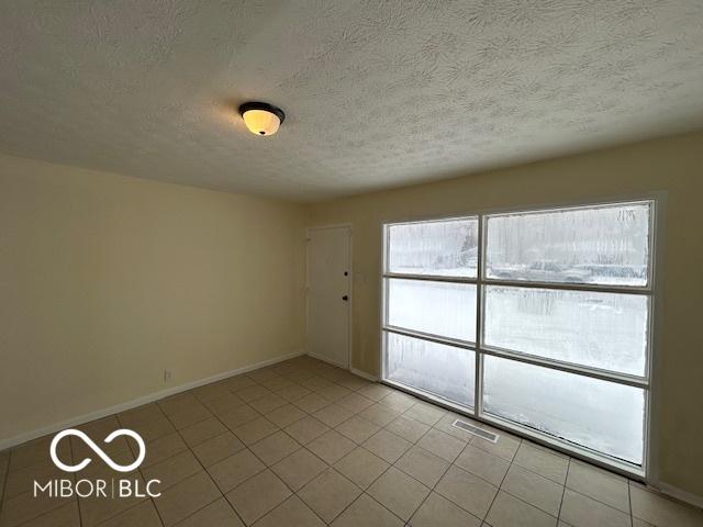 empty room with light tile patterned floors, visible vents, baseboards, and a textured ceiling