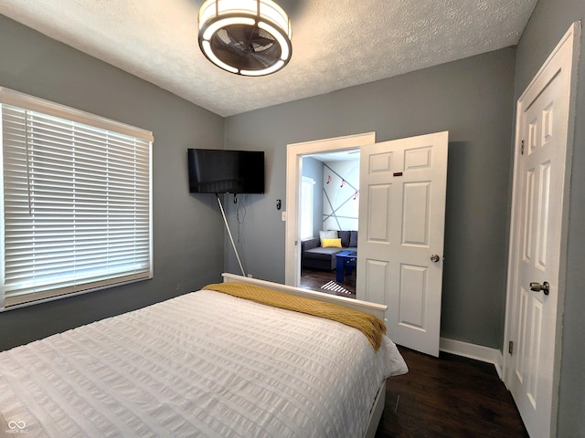 bedroom with dark wood-style flooring, a textured ceiling, and baseboards