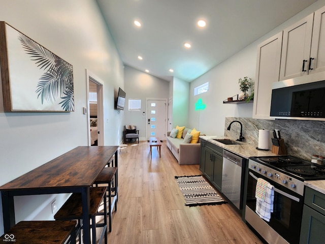 kitchen with appliances with stainless steel finishes, light wood-style floors, a sink, and light stone counters