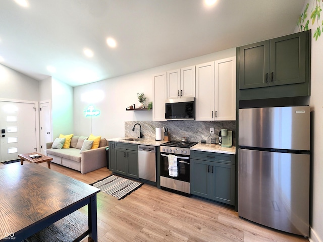 kitchen with a sink, white cabinets, light wood finished floors, appliances with stainless steel finishes, and tasteful backsplash