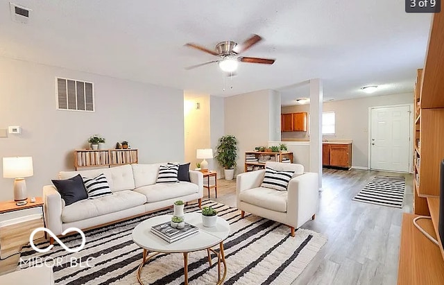 living area featuring light wood-type flooring, ceiling fan, visible vents, and baseboards