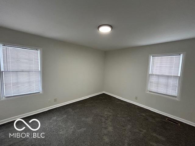 unfurnished room with baseboards, visible vents, and dark carpet