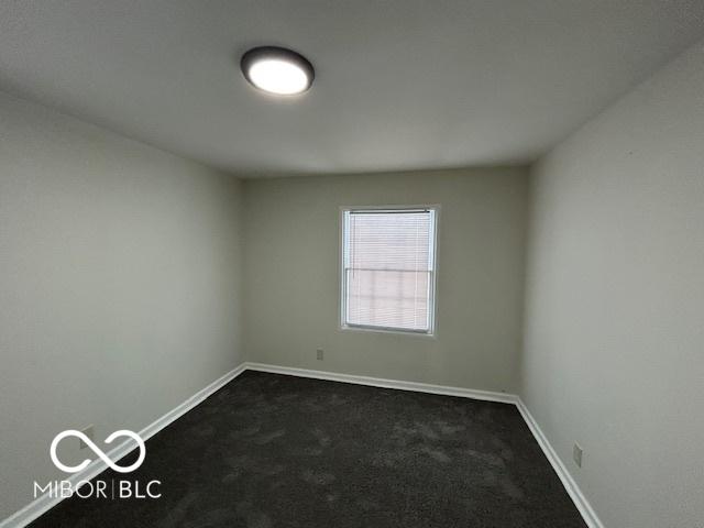 unfurnished room featuring baseboards and dark colored carpet