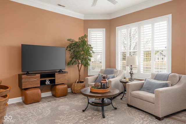 living area featuring light wood-style floors, ceiling fan, visible vents, and crown molding