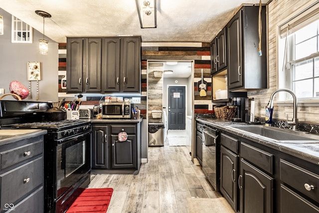 kitchen featuring decorative light fixtures, dark countertops, light wood-style flooring, a sink, and black appliances