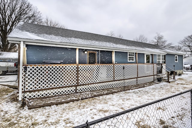 snow covered back of property with fence and roof with shingles