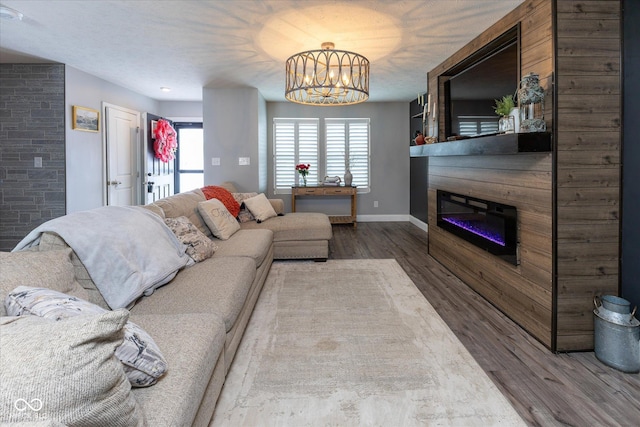 living area with a textured ceiling, wood finished floors, baseboards, a glass covered fireplace, and an inviting chandelier