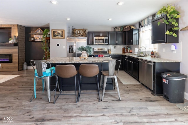 kitchen with a kitchen island, appliances with stainless steel finishes, light stone counters, and a sink