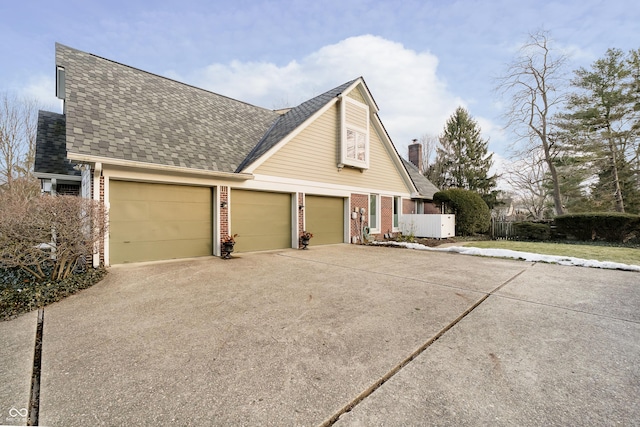 view of property exterior featuring driveway, a chimney, roof with shingles, an attached garage, and brick siding