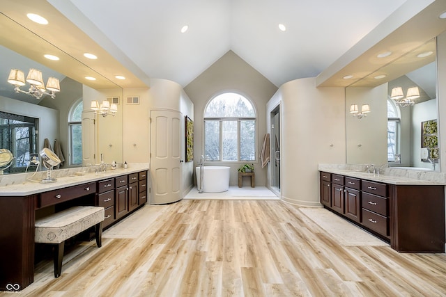 full bath featuring visible vents, lofted ceiling, wood finished floors, a freestanding bath, and vanity