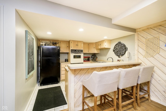 kitchen with a kitchen breakfast bar, white oven, freestanding refrigerator, light countertops, and light brown cabinets