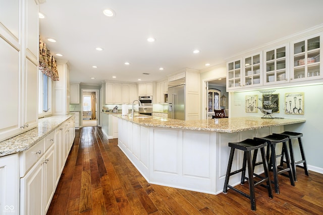 kitchen with built in refrigerator, light stone countertops, glass insert cabinets, and white cabinets