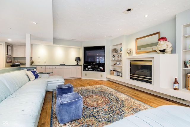 living room featuring light wood-type flooring, recessed lighting, built in features, and a glass covered fireplace