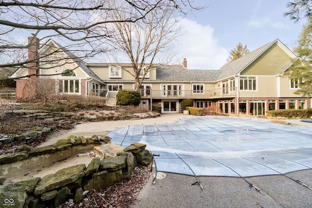 rear view of property with brick siding, a covered pool, a chimney, and a patio