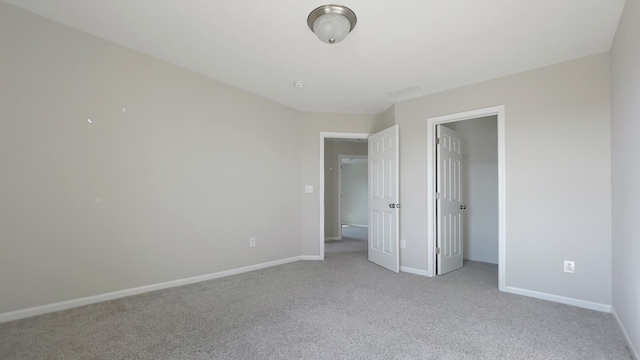 unfurnished bedroom featuring light carpet, a spacious closet, a closet, and baseboards