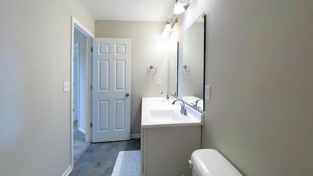 bathroom with a sink, baseboards, toilet, and double vanity