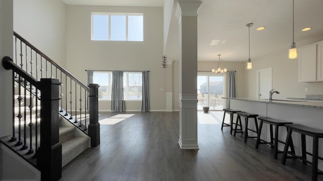 entryway featuring stairs, dark wood-type flooring, decorative columns, and a chandelier