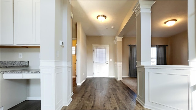 hall featuring baseboards, dark wood finished floors, and ornate columns