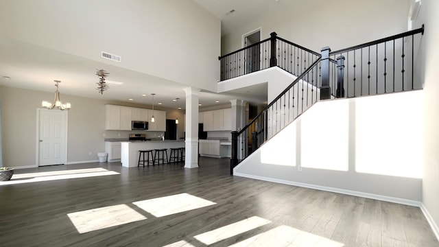 unfurnished living room featuring dark wood finished floors, baseboards, visible vents, and ornate columns