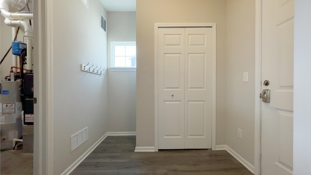 hallway with water heater, visible vents, dark wood-type flooring, and baseboards