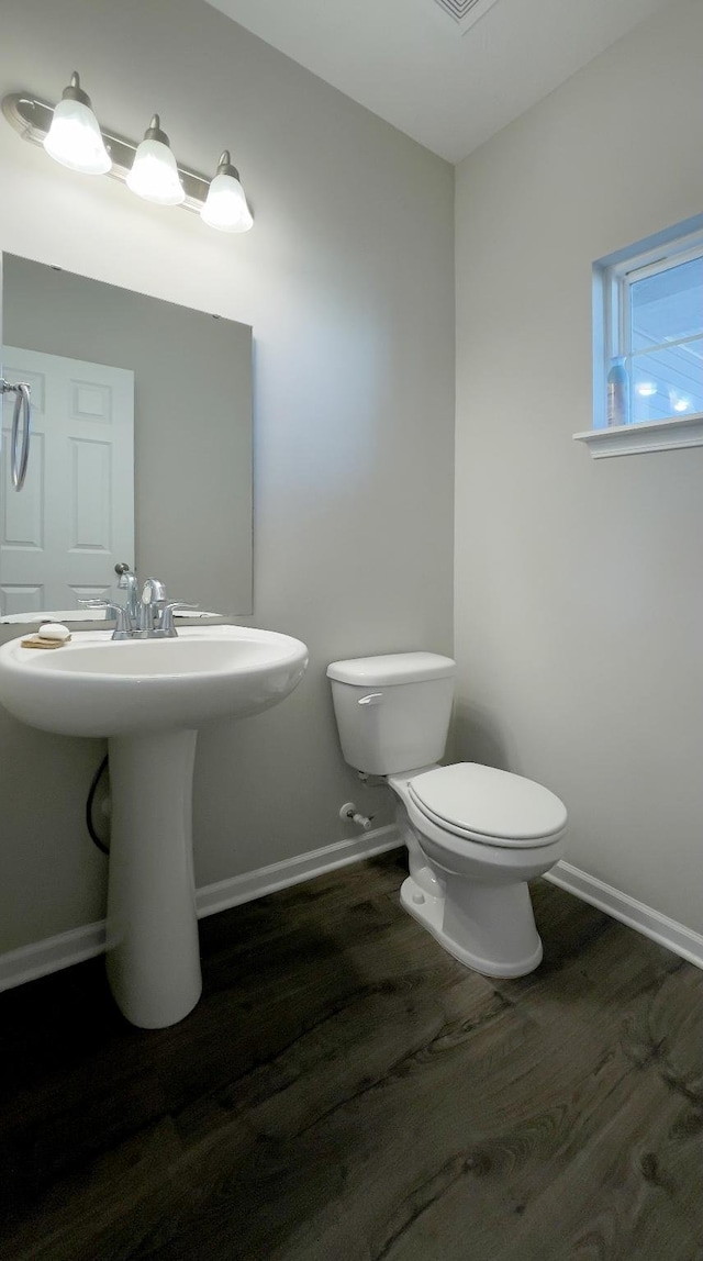 half bath with baseboards, toilet, and wood finished floors