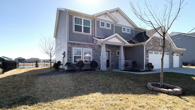 craftsman-style house with stone siding, fence, concrete driveway, a front yard, and a garage