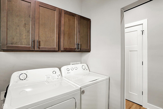 clothes washing area featuring light wood-style floors, washing machine and dryer, and cabinet space