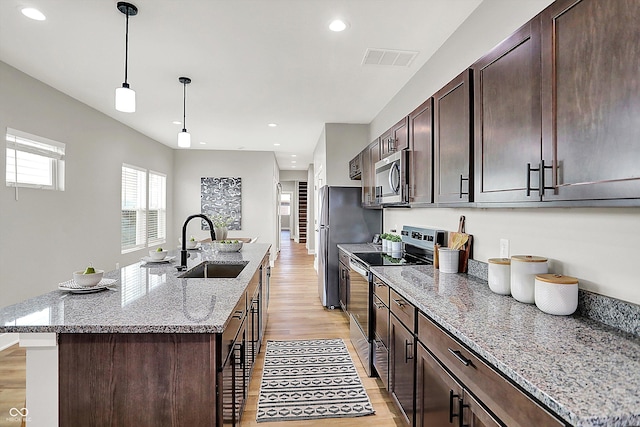 kitchen with a center island with sink, visible vents, appliances with stainless steel finishes, dark brown cabinetry, and a sink