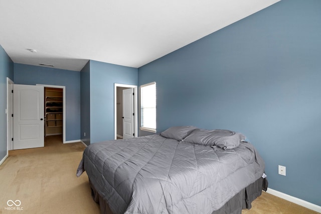 bedroom featuring light carpet, a walk in closet, and baseboards