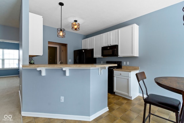 kitchen with white cabinets, light countertops, black appliances, a kitchen bar, and pendant lighting