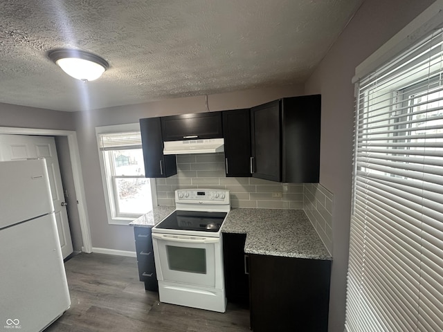 kitchen featuring backsplash, light stone countertops, dark cabinets, white appliances, and under cabinet range hood