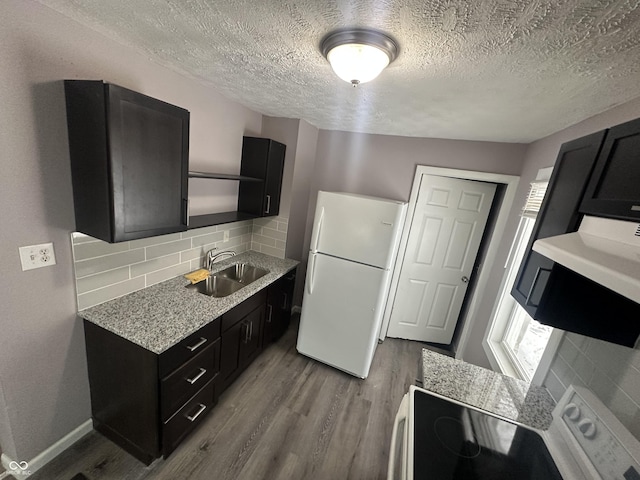 kitchen featuring dark cabinetry, stainless steel range with electric stovetop, a sink, and freestanding refrigerator