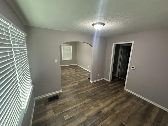 spare room featuring arched walkways, a textured ceiling, dark wood-type flooring, visible vents, and baseboards