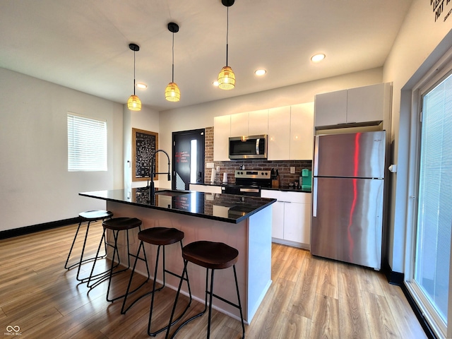 kitchen featuring stainless steel appliances, dark countertops, hanging light fixtures, an island with sink, and modern cabinets